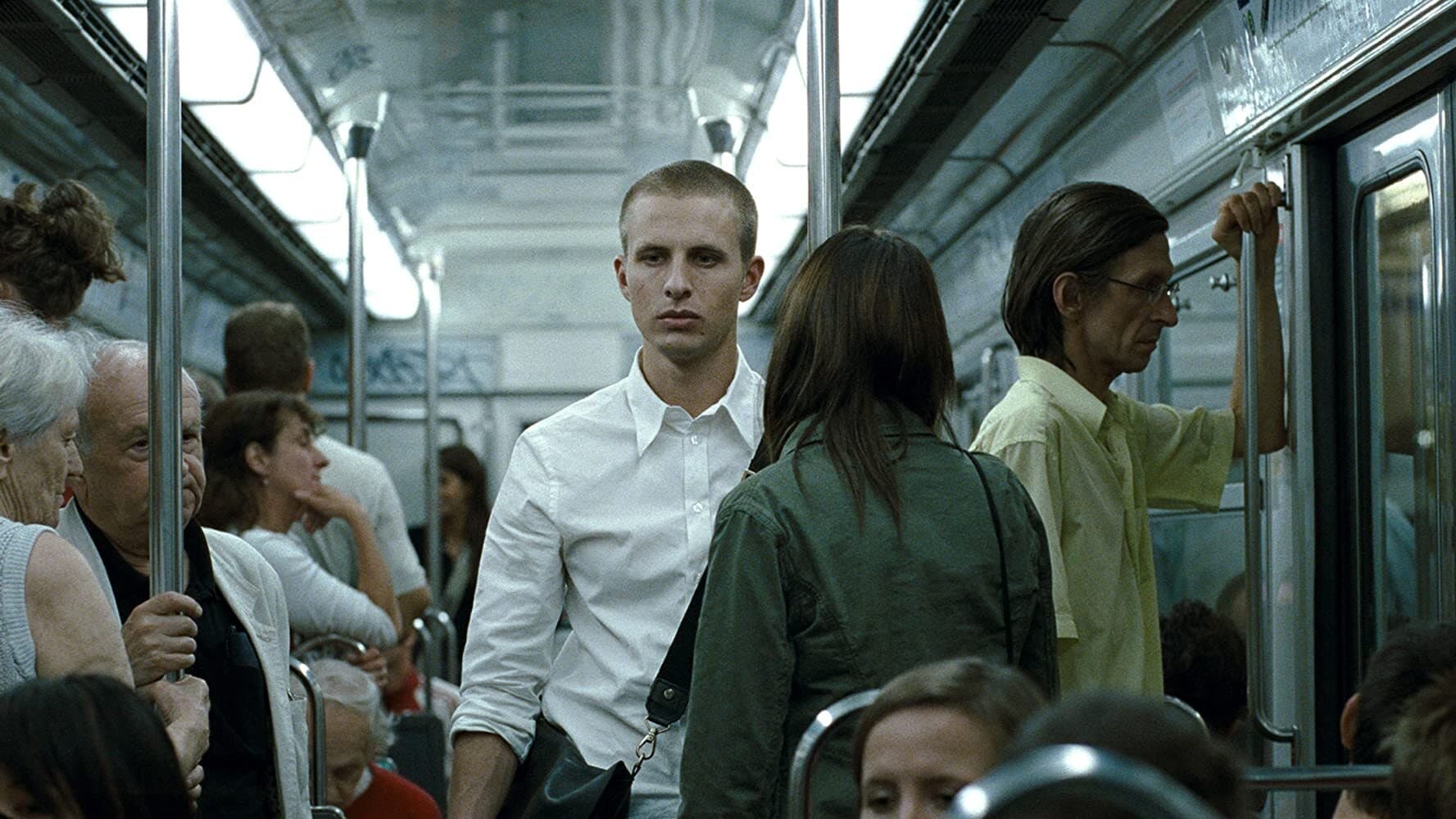 Still from Reprise by Joachim Trier. Protagonist Philipp is pictured wearing a white shirt on the bus, among other passengers. He is looking slightly down and to the side, not straight at the camera, and seems lost in thought.